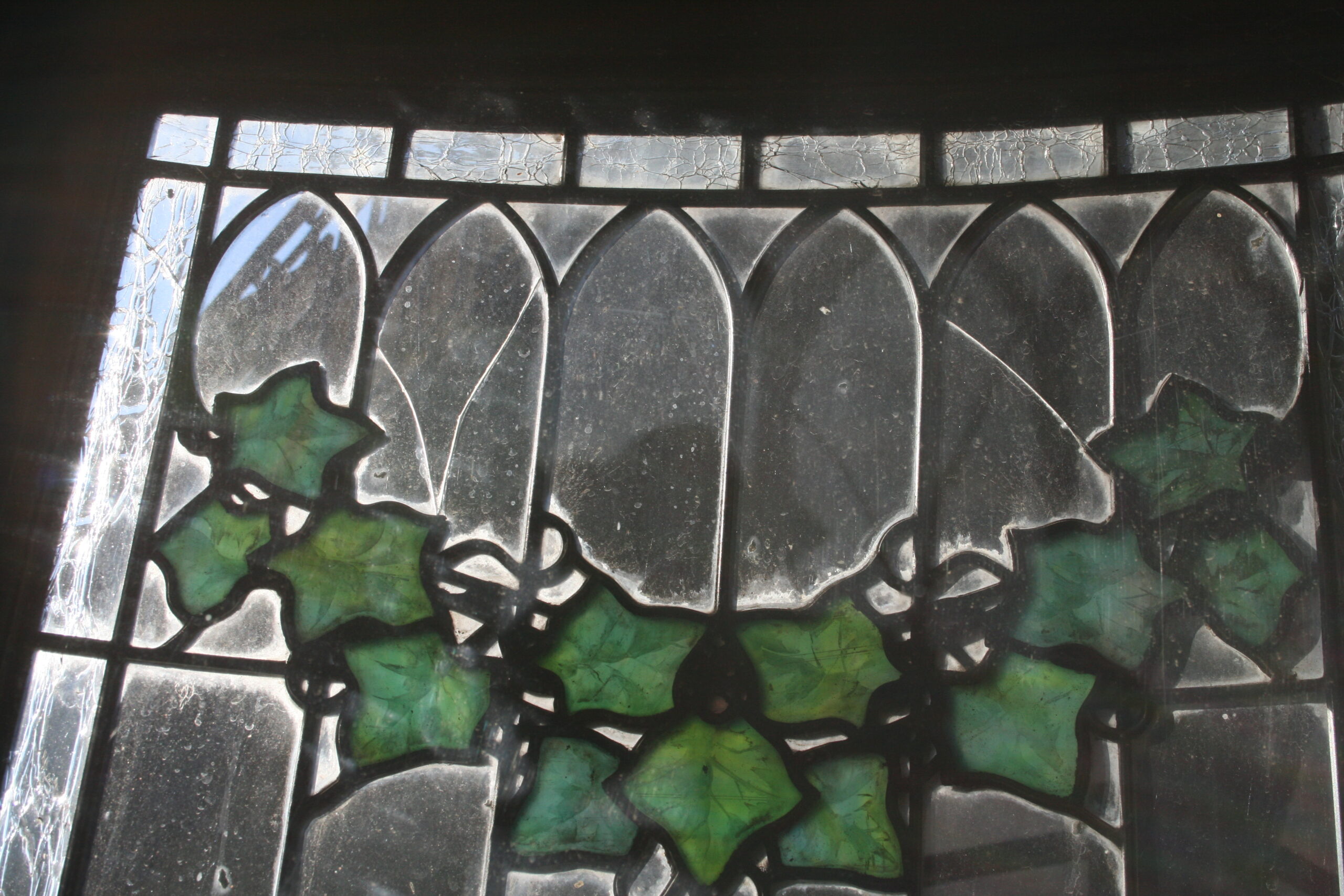 A detail photograph of the painted and fired ivy detail, as well as cracked clear glass, prior to restoration.