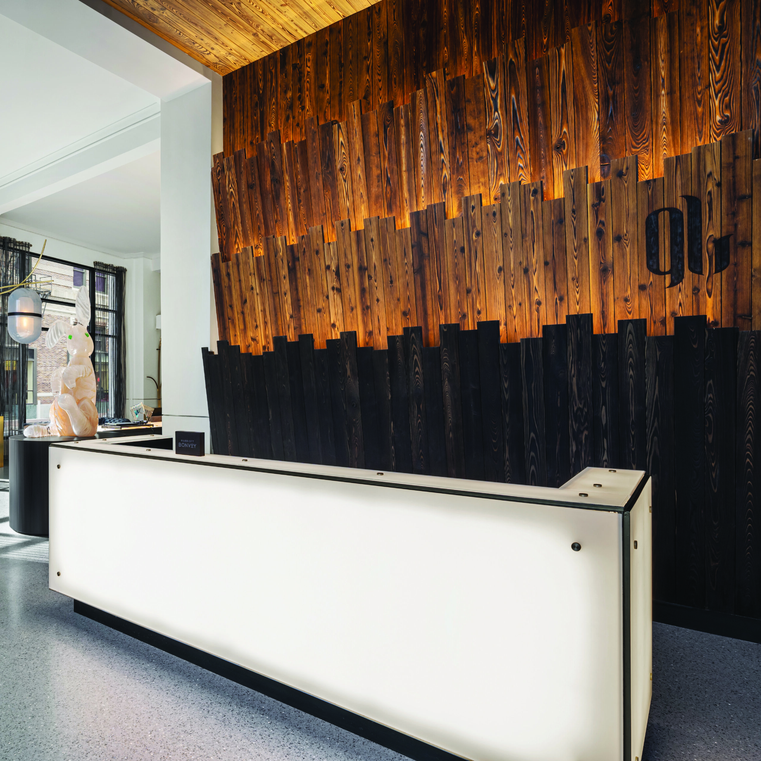 white reception desk in the foreground with a multi-colored wood wall and a glass sculpture of a rabbit in the background.